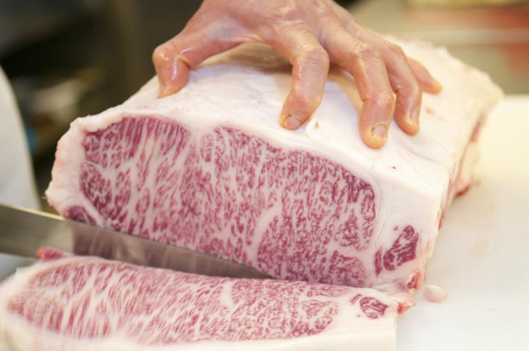 大きな霜降り肉を包丁で切っている画像